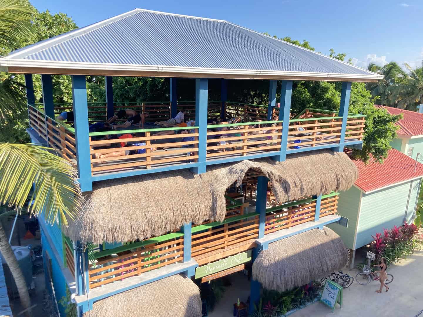 An bright blue and green open air building with a rooftop and people doing yoga on the top floor.