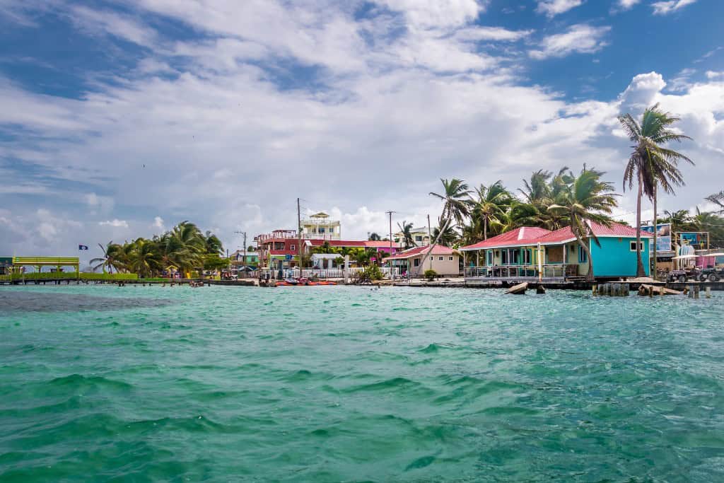 A emerald colored ocean with an island with brightly colored buildings and palm trees in the background.