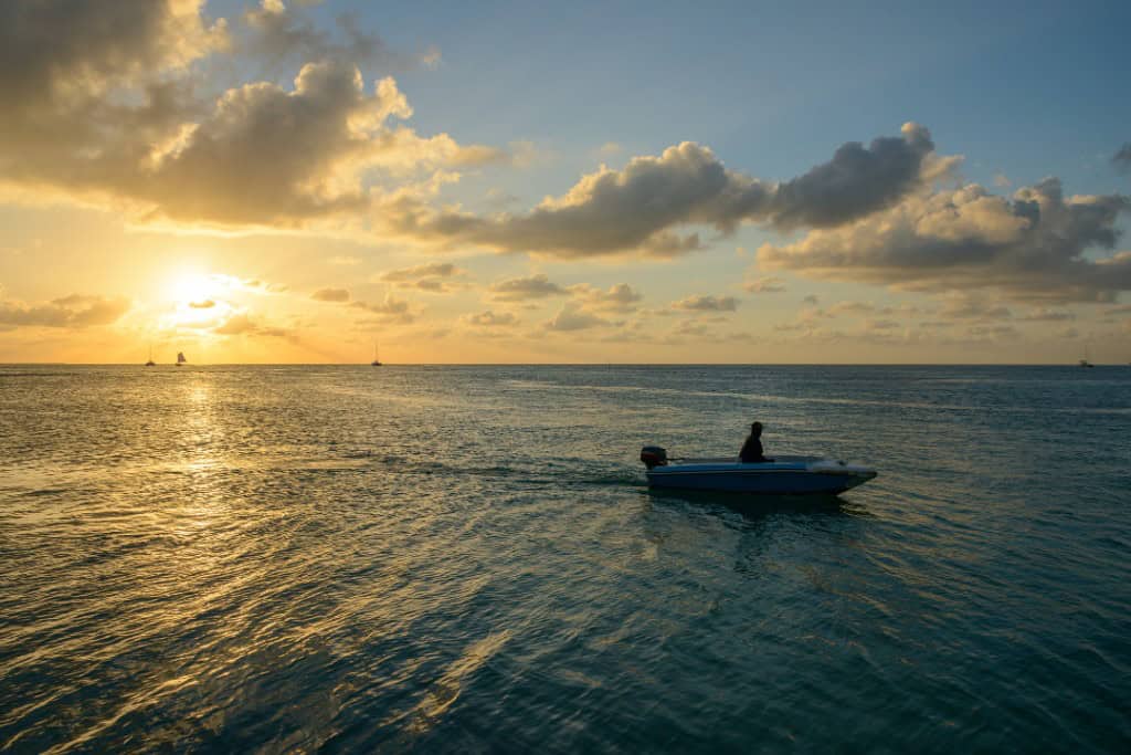 A speed boat in the ocean with the sun setting off to the side behindit