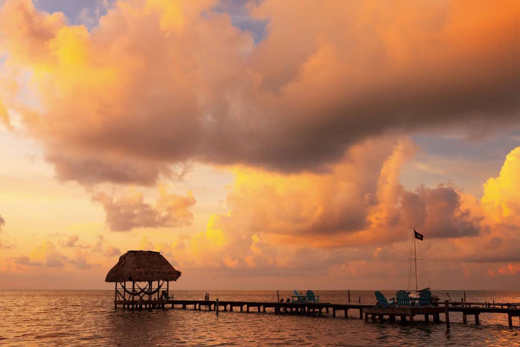 A long dock with a beautiful yellow and orange sunrise in a sky full of clouds in the background