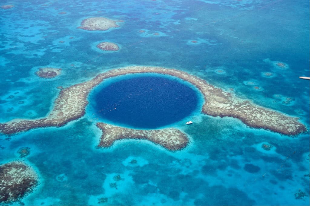 An aerial shot of a dark blue hole in the ocean with reefs surrounding it