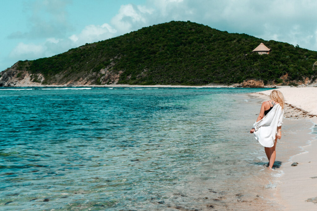 Blonde woman in white cover up walking along the edge of a turquoise ocean on Scrub Island BVI