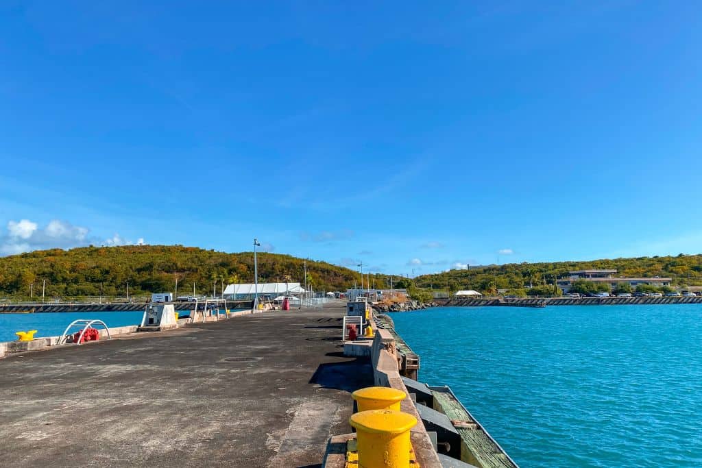 A concrete ferry terminal on brightly turquoise water with rolling green hills in the background.