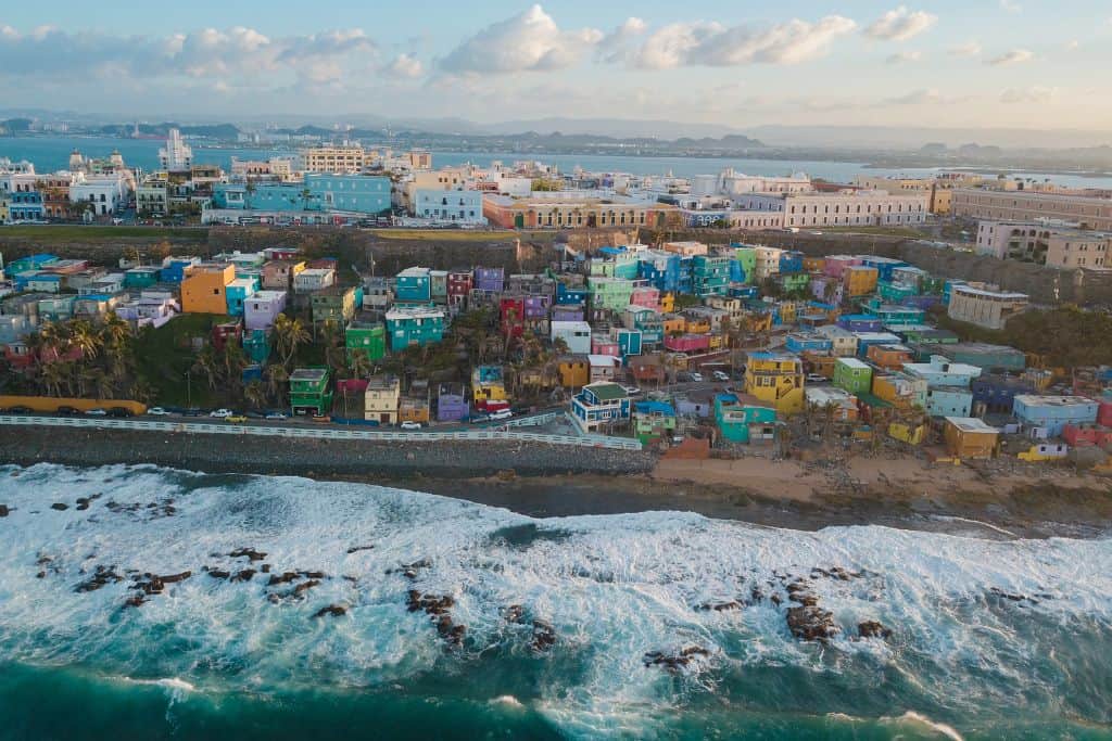 An aerial shot of many colorful houses and businesses along a rocky coastline with a rocky sea below them.