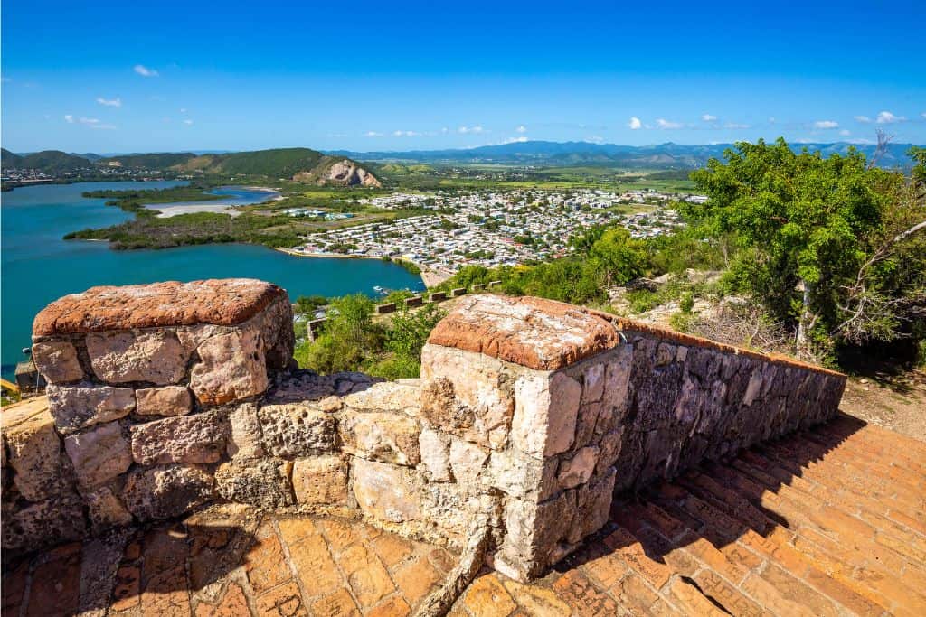 White and red stone staircase ruins over looking a beautiful view of the ocean, a town and mountains.