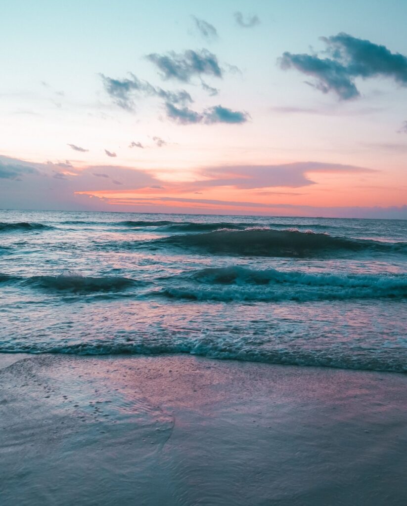 turquoise colored waves with a pink and orange sunrise reflecting on the waters and some dark blue clouds in the sky