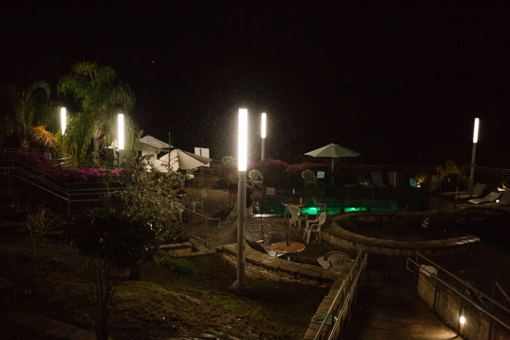 A garden area with a pool, seating area, stairs and gardens lit up at night