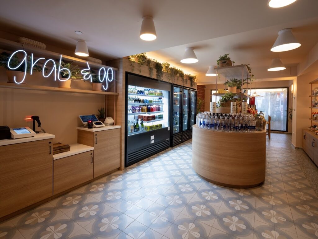 A small store with the words grab & go in neon on the left next to a large black refrigerator display and a wooden display holding alcohol in the center of the room.