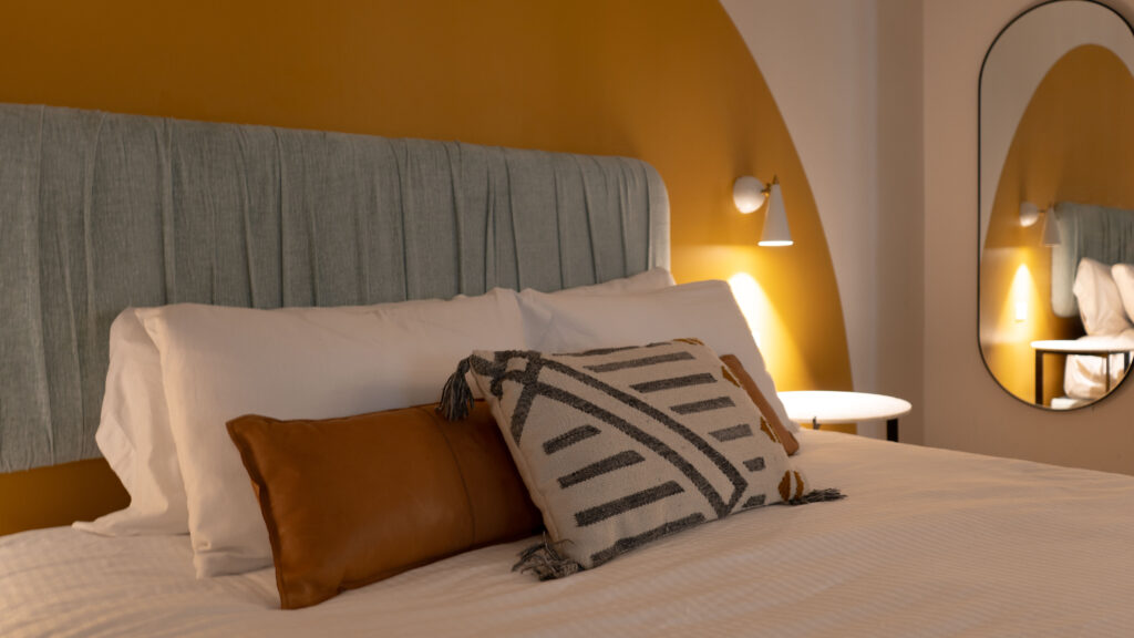 A bed with a blue and white striped and brown pillows on it against the light blue headboard and a yellow circle painted on the wall behind it.