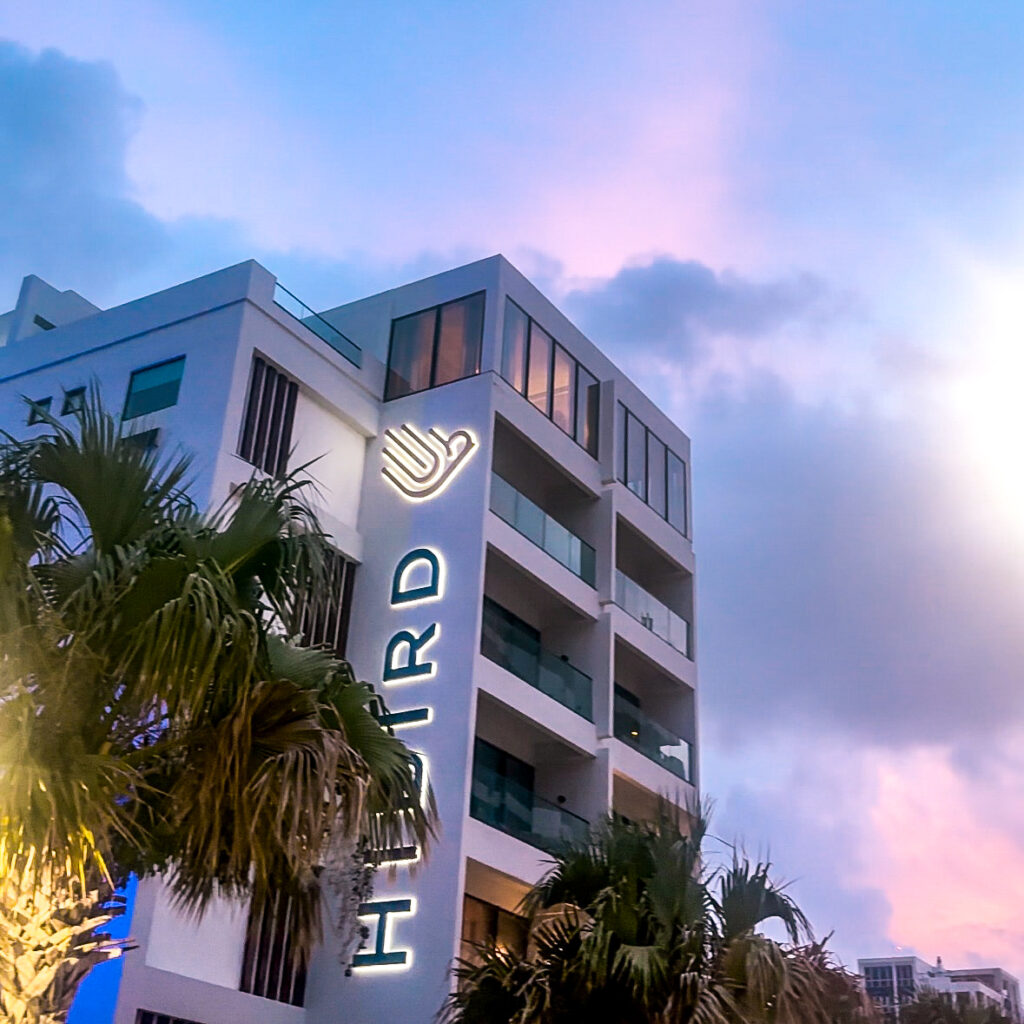 A cotton candy colored sky with a hotel that says Hibird with a palm tree in front of it