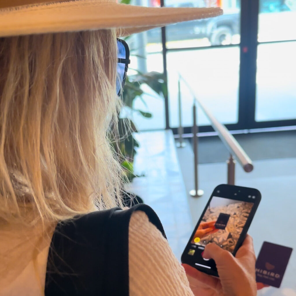 A woman with a hat, sunglasses and pink fingernails looking at her phone at an app