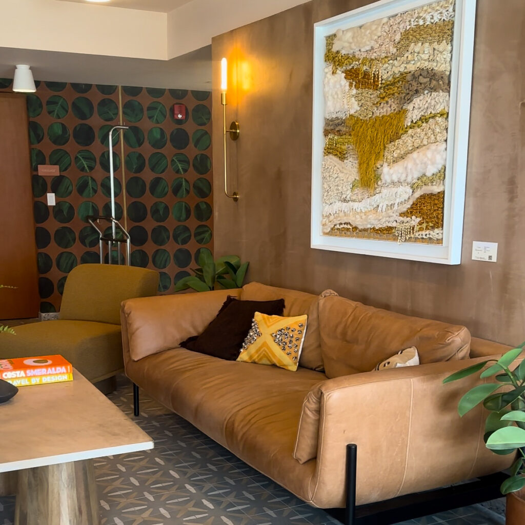 A brown couch leather with textured pillows and gold and white textile artwork in a hotel lobby