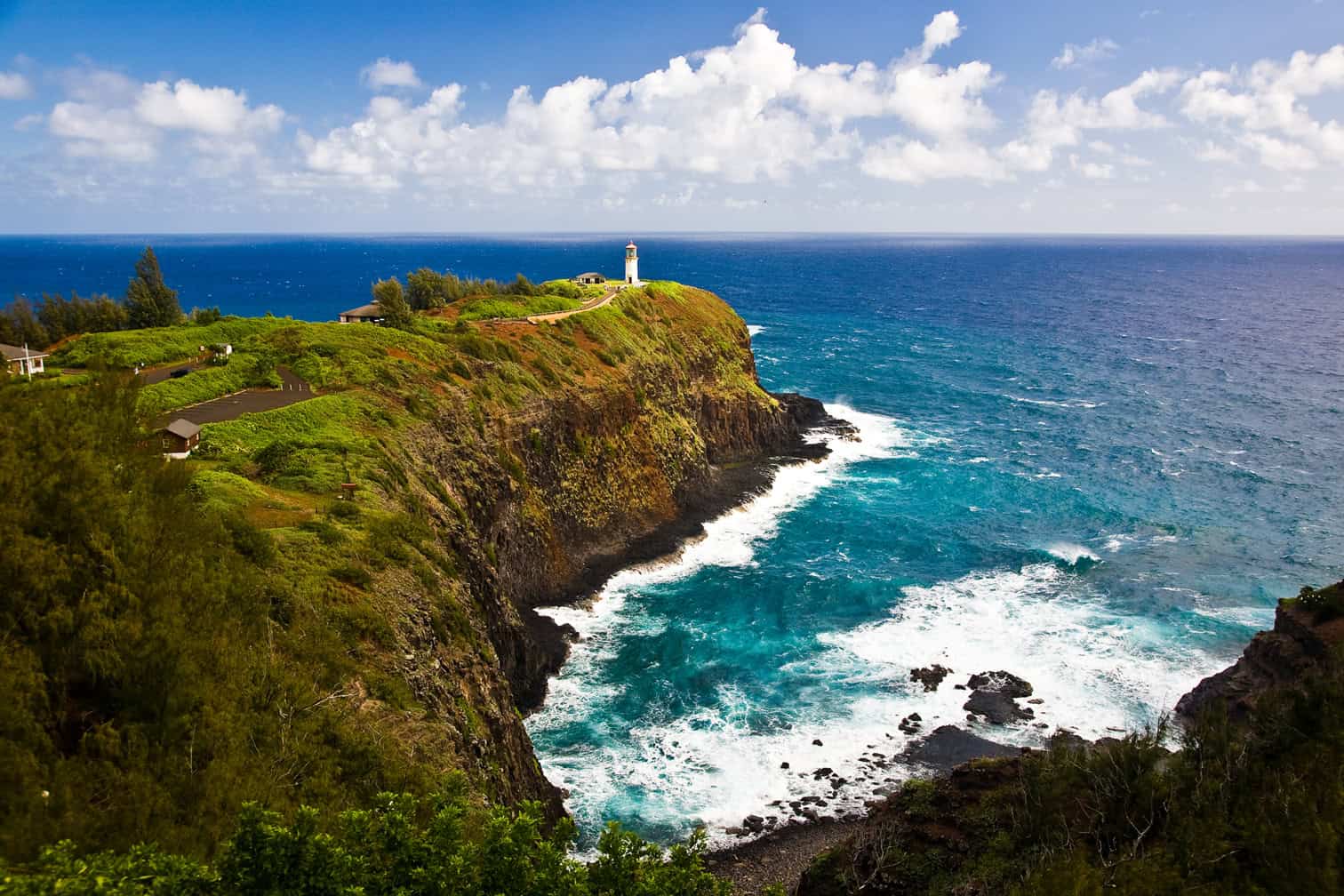 A white lighthouse sitting on a tall green cliff overlooking a turquoise ocean in Kauai