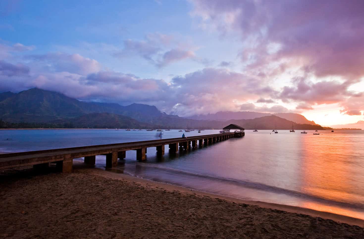 A cotton colored sunset behind a pier sticking out into Hanalei Bay in Kauai