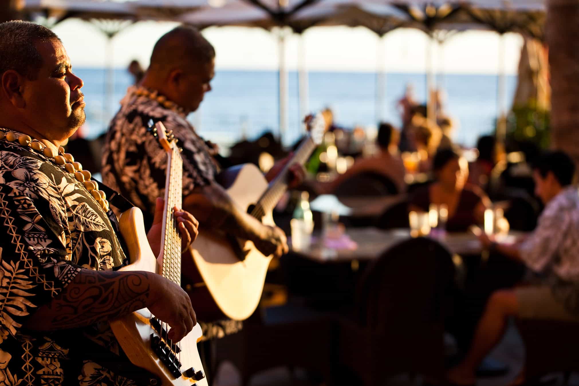 Two men playing the guitar to ocean front diners in the distance