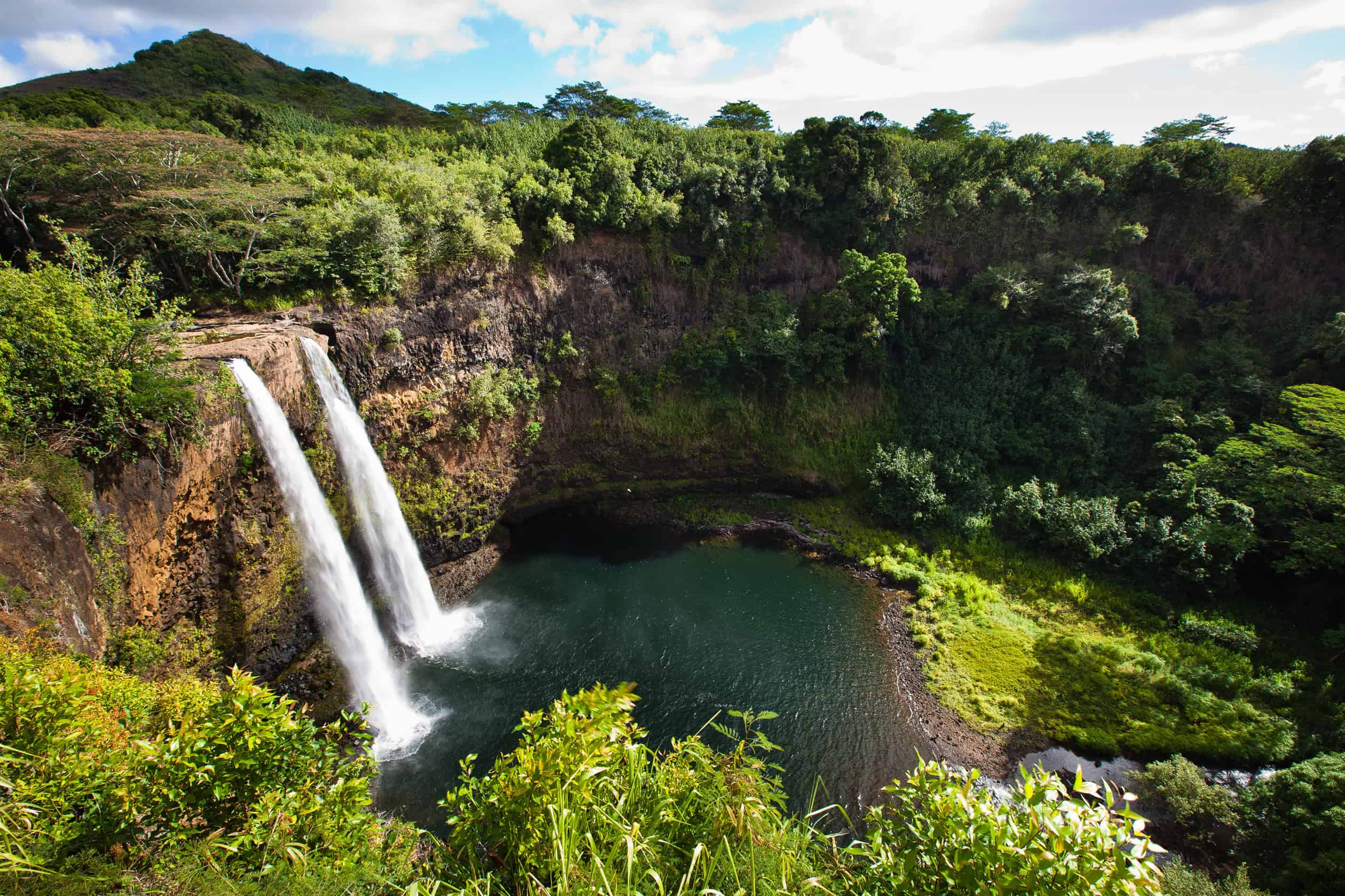 Twin waterfalls cascading down foliage filled clips, landing in a deep green lake.