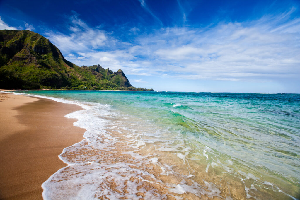 A tropical beach with turquoise waters and cliffs in the background in Kauai