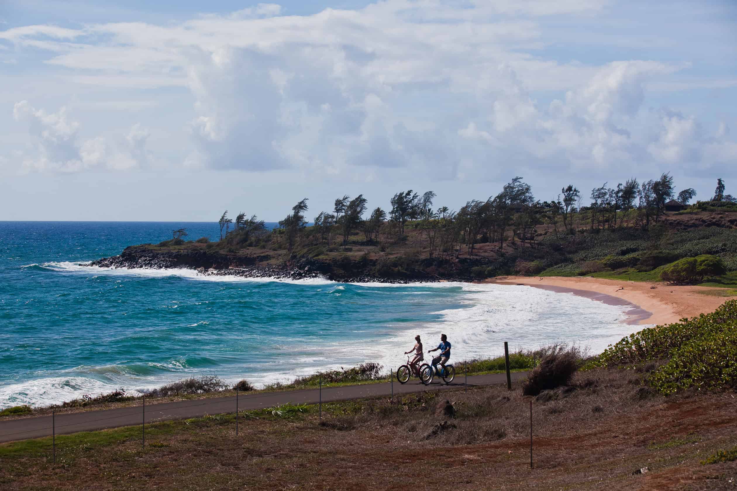 Two people biking along the ocean in Kauai