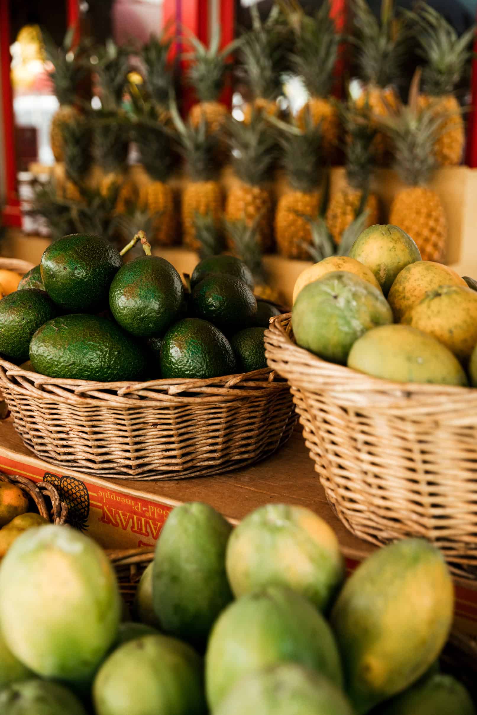 A fruit stand with a line of pineapples, avocados and other tropical fruits in baskets in Kauai.