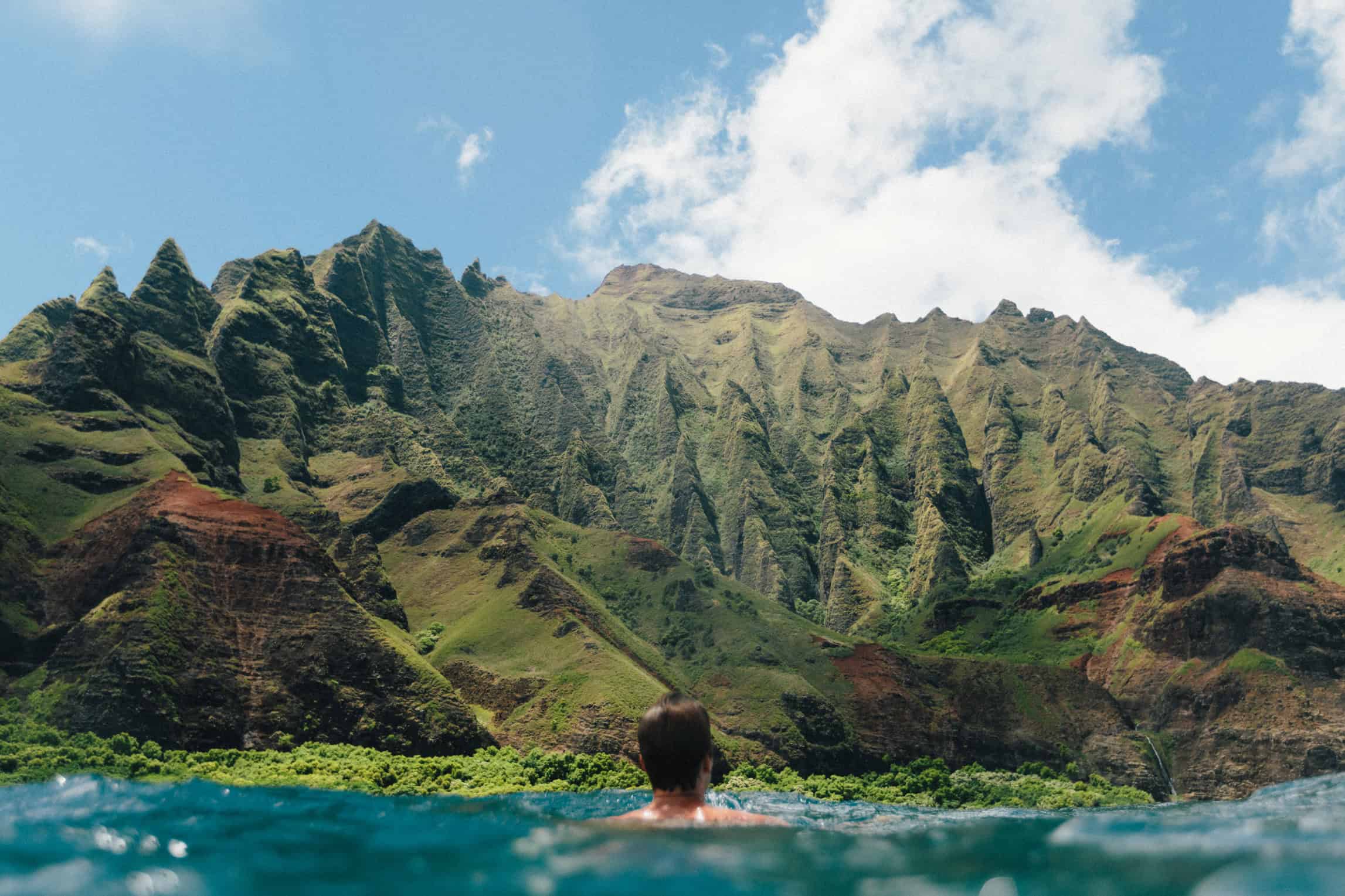 A man swimming in the ocean looking out at a mountainous landscape