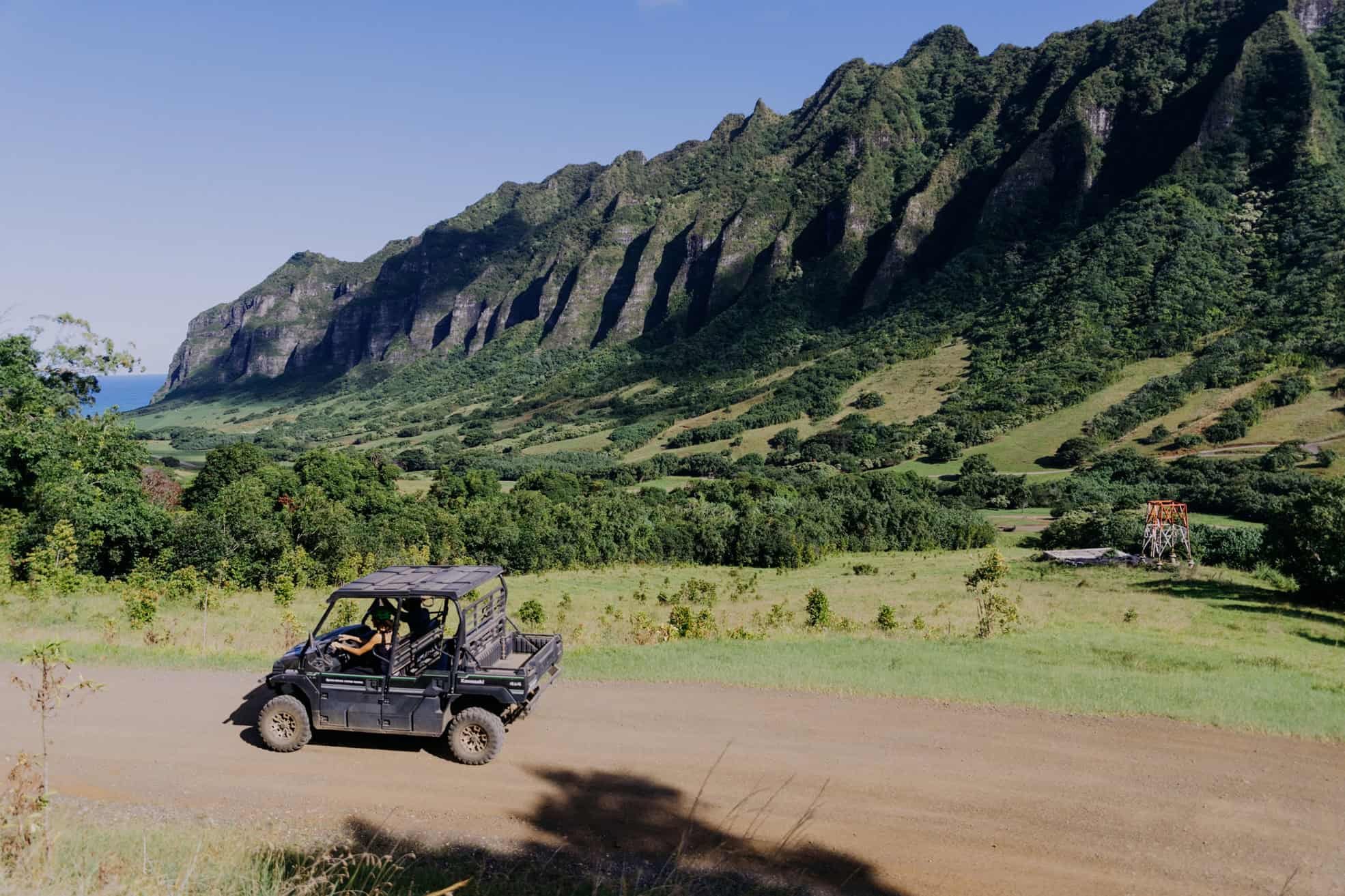 A green ATV on a dirt road, with a tall beautiful mountain with trees on it in the background