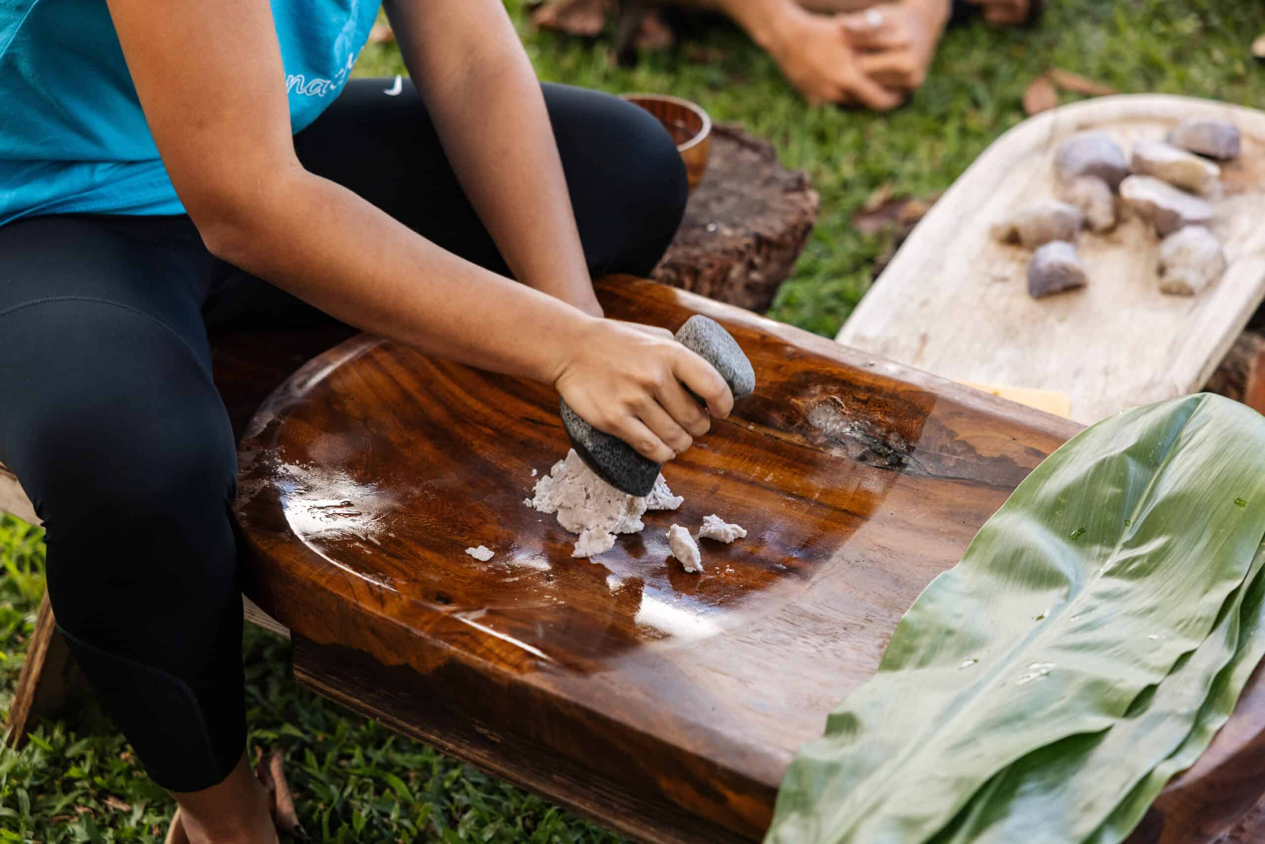 A woman in a blue shirt leaning over a wooden table, pounding poi