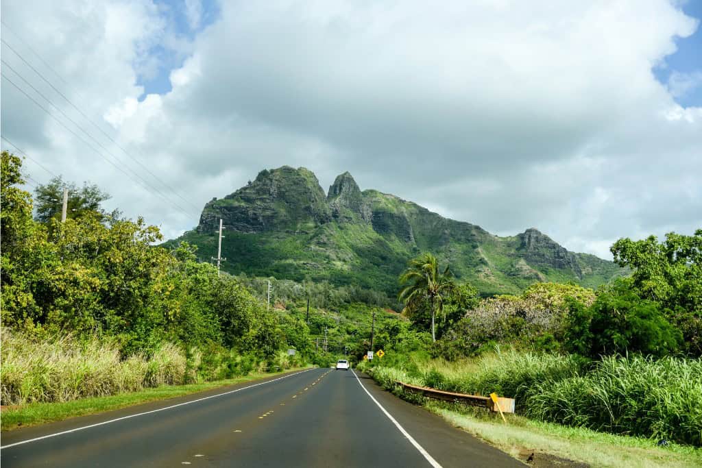 An open road leading towards tall foliage filled mountains in Kauai