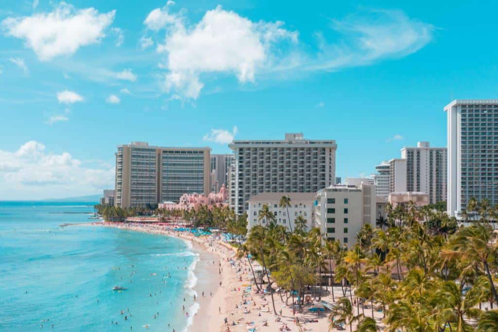 An aerial shot of a beach with a city behind it and lots of people on the beach and in the water