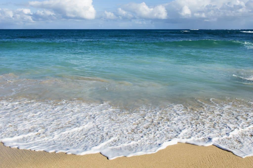 White and light turquoise waves lapping up on a yellow shore.