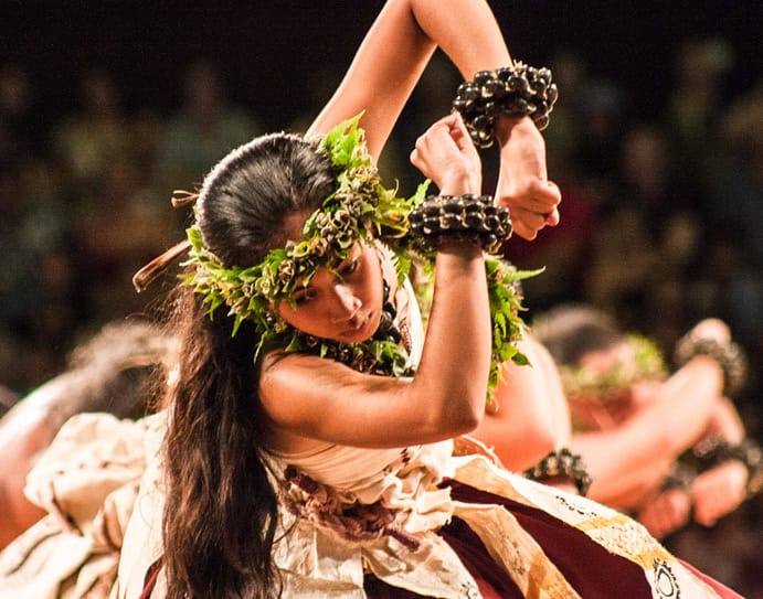 A Polynesian woman with long dark hair and a plant headset, wearing a traditional white uniform performing a hula dance