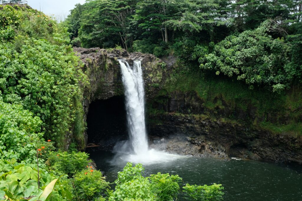 A waterfall cascading off a tall cliff into dark blue water with lush forest all around