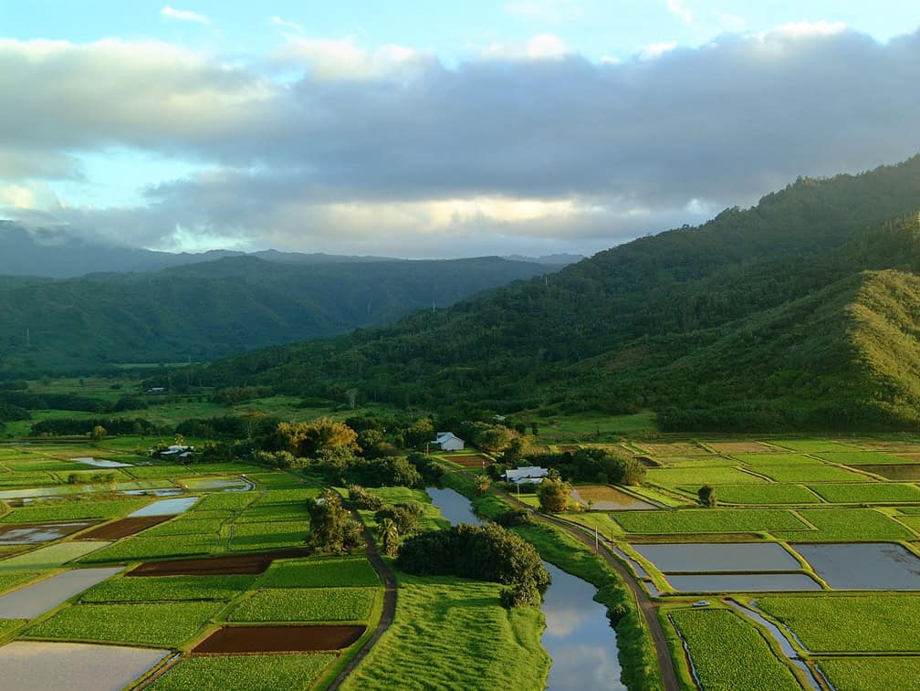 A valley with a calm river and farm, and mountains in the background