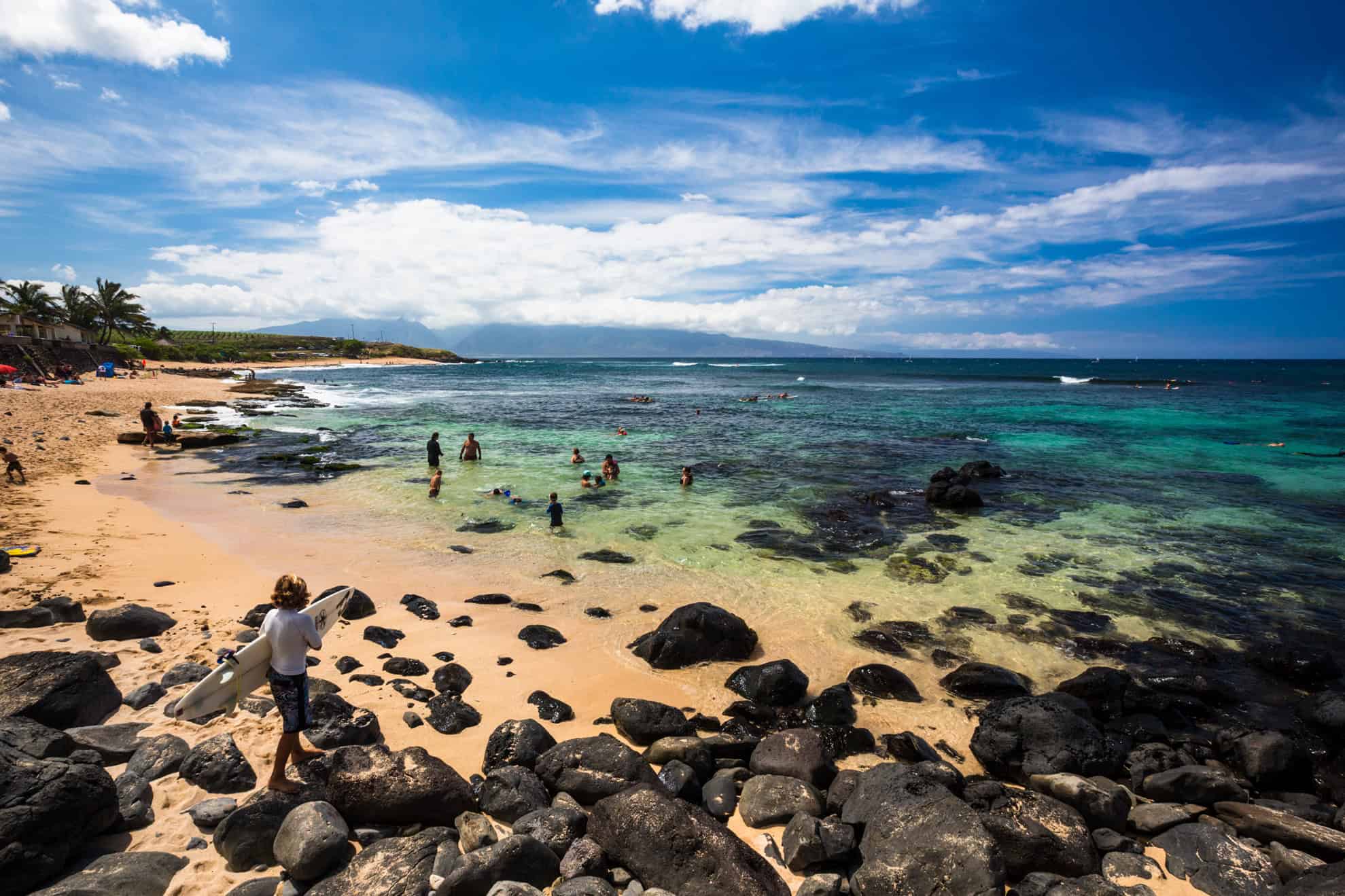 A rocky beach with calm waters and people snorkeling