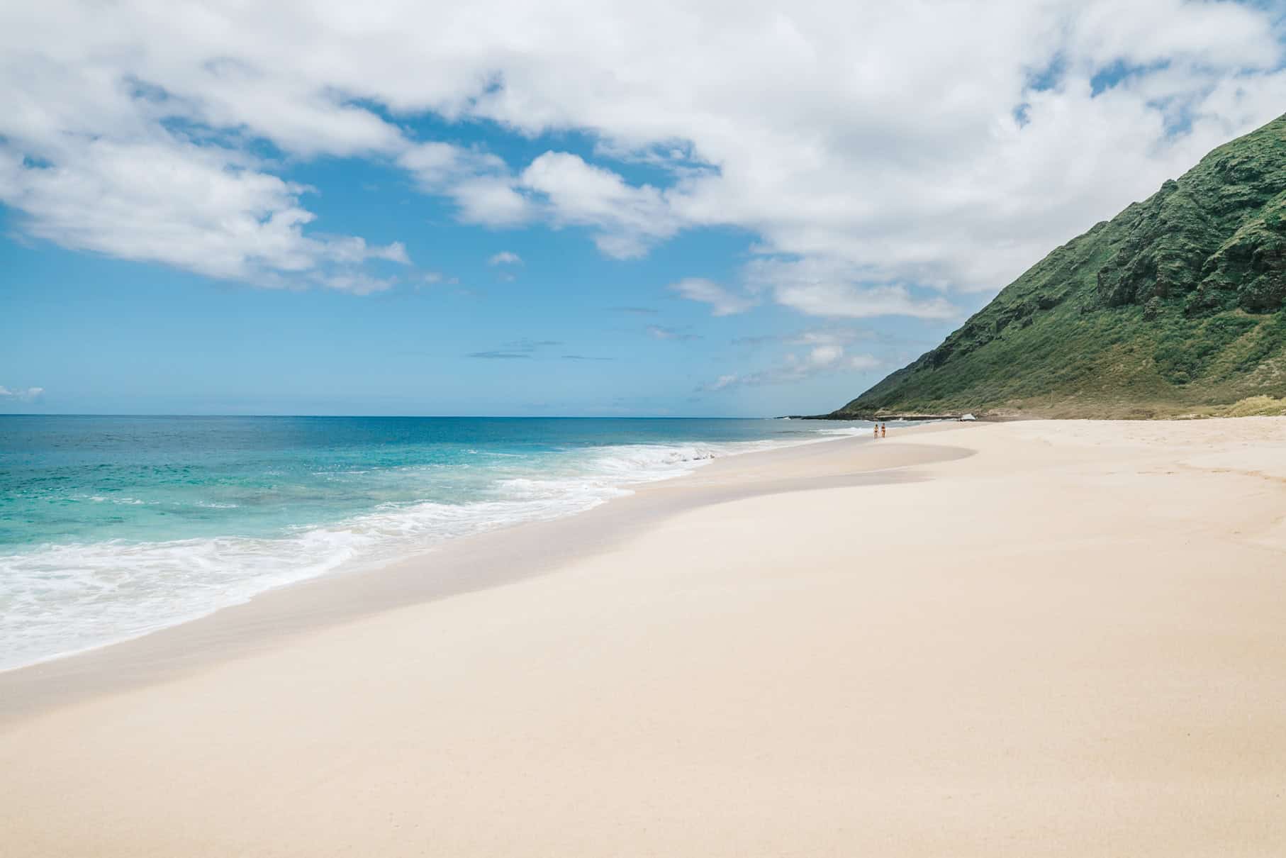 A white sand beach with a turquoise ocean to the left and green mountains to the right.