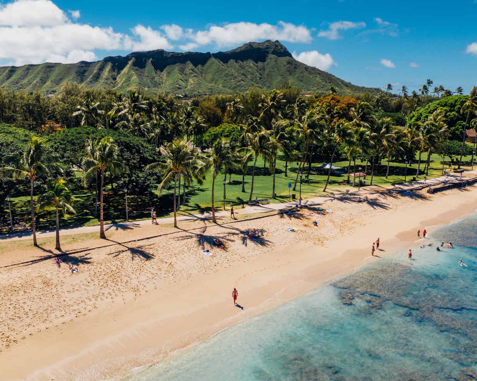 A bright beach with calm water and a tall green mountain in the background