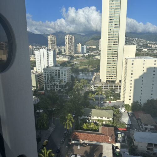 A view of a tropical city with white high rise buildings scattered in the foreground, mountains and clouds in the background