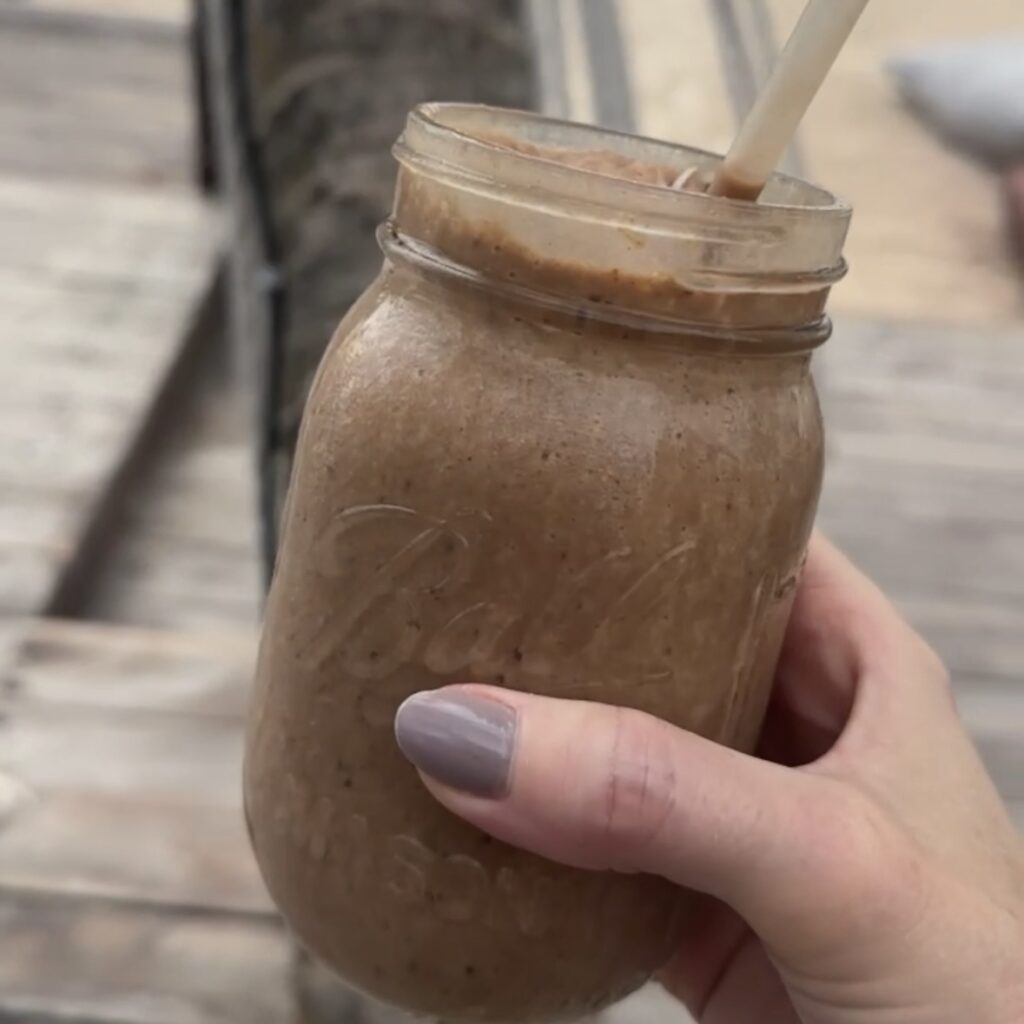 A woman's hand holding a brown smoothie in a glass