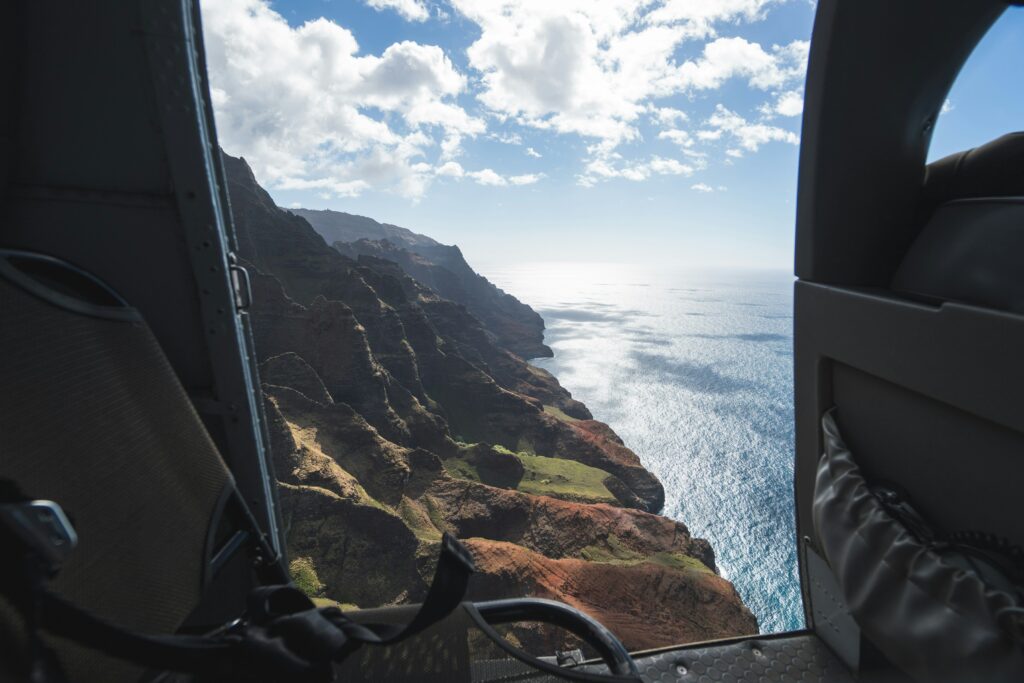 An open helicopter door looking down at a view of mountains rolling into an ocean