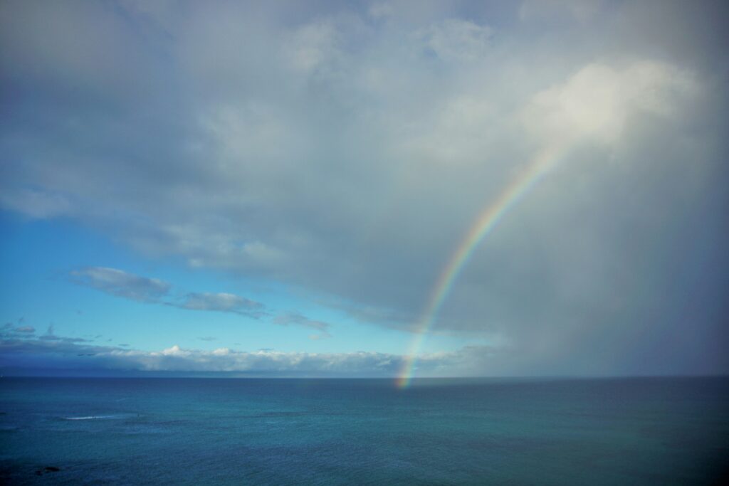 A dark blue ocean with a cloudy sky and rainbow from the clouds to the ocean