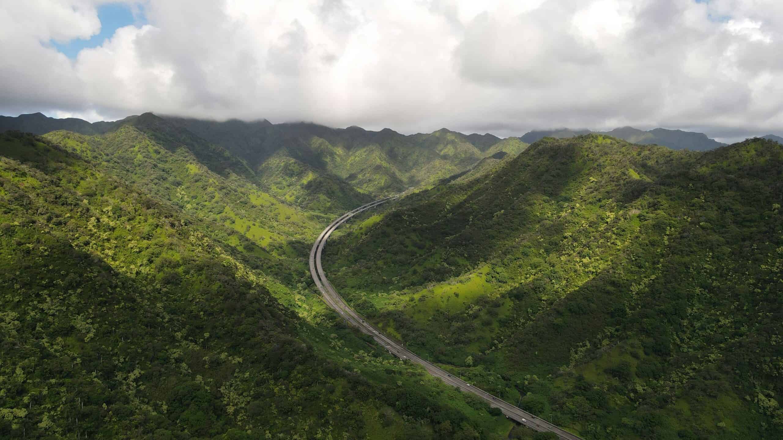 Green mountains with a highway running through the valley and a white cloudy sky