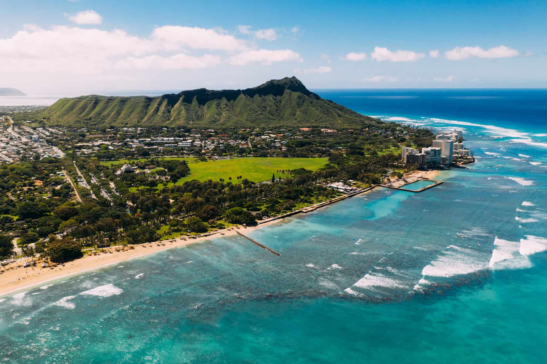 An aerial shot over the ocean looking towards a tall mountain with a town at its valley