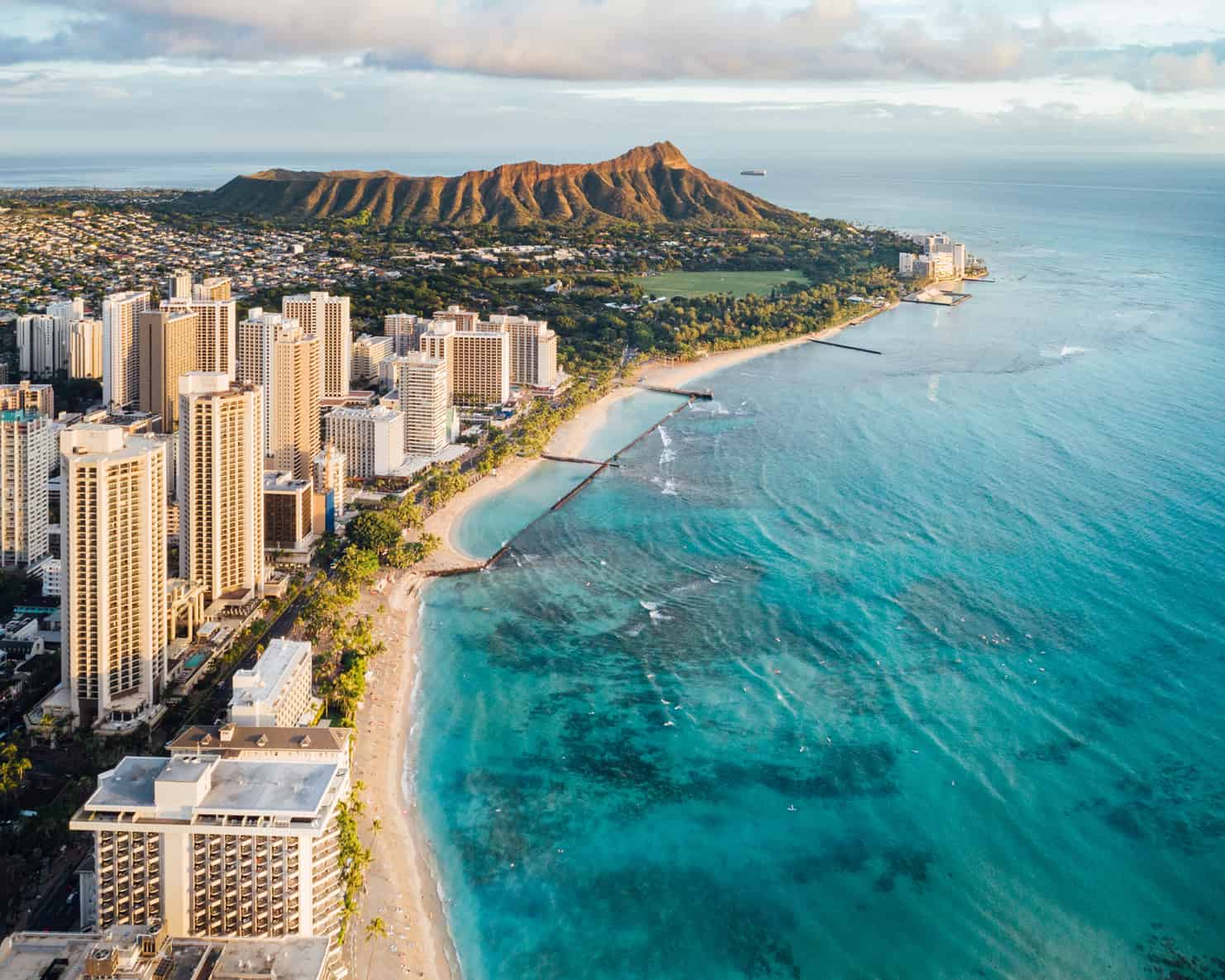 An aerial view of a Waikiki with a turquoise ocean on the right and Diamond Head in the background