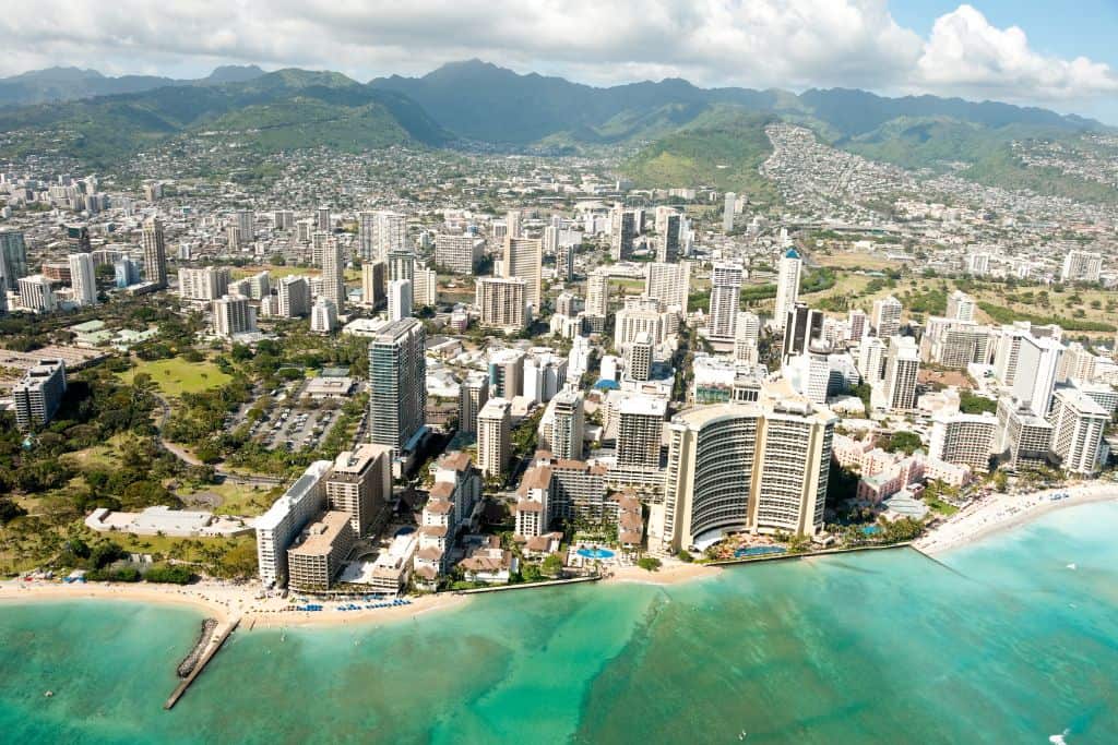 An aerial view of a congested city against the ocean with mountains in the background.