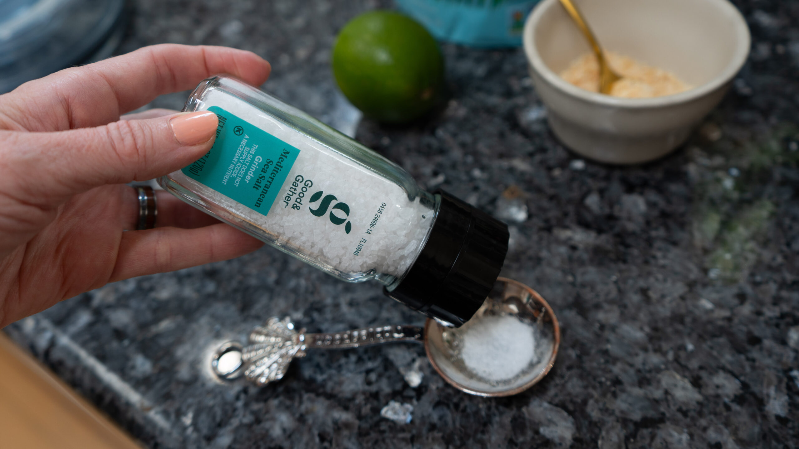 A bottle of Good & Gather Sea Salt being poured into a measuring spoon