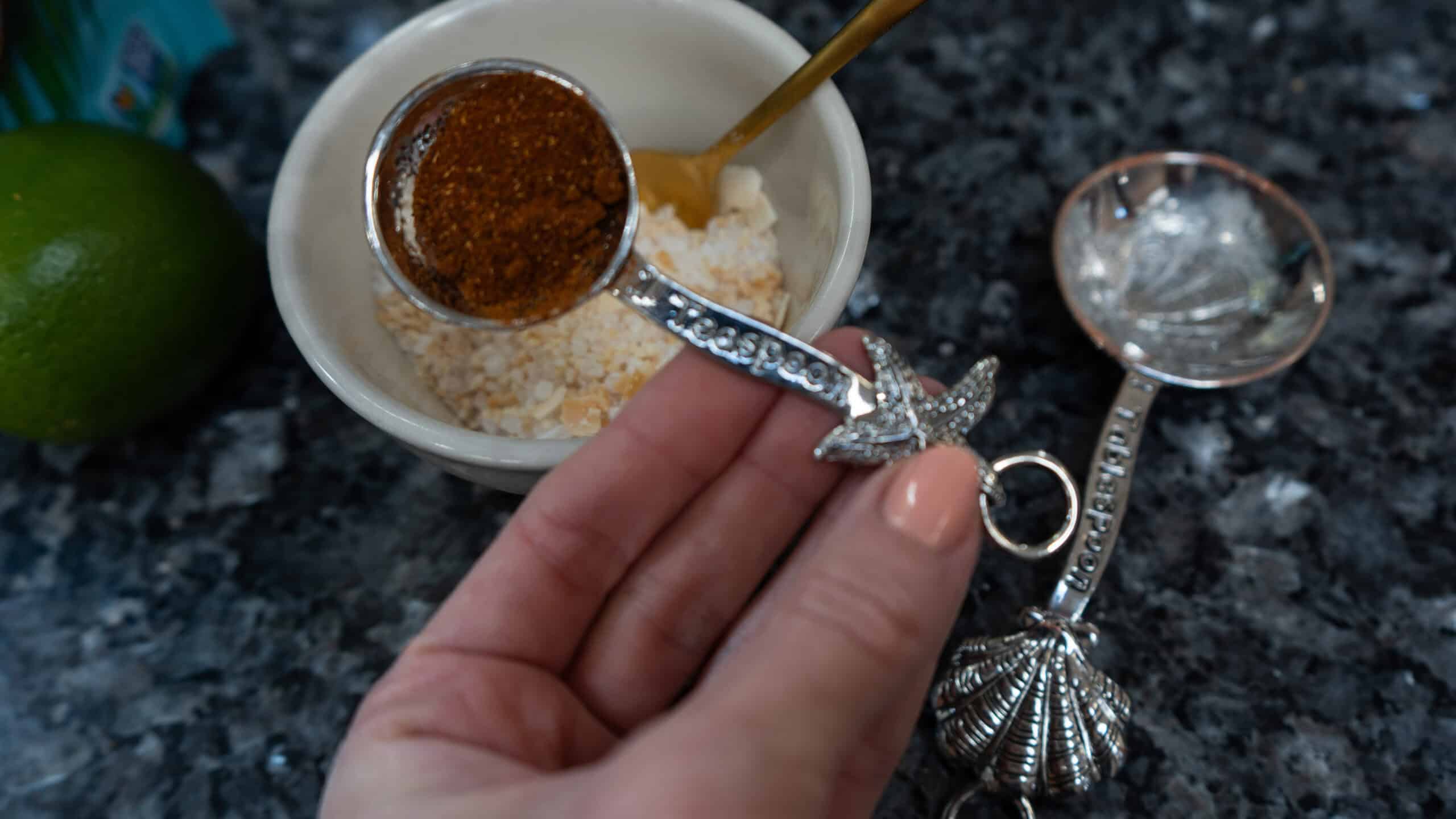 A teaspoon full of a red powder over a bowl of white herbs