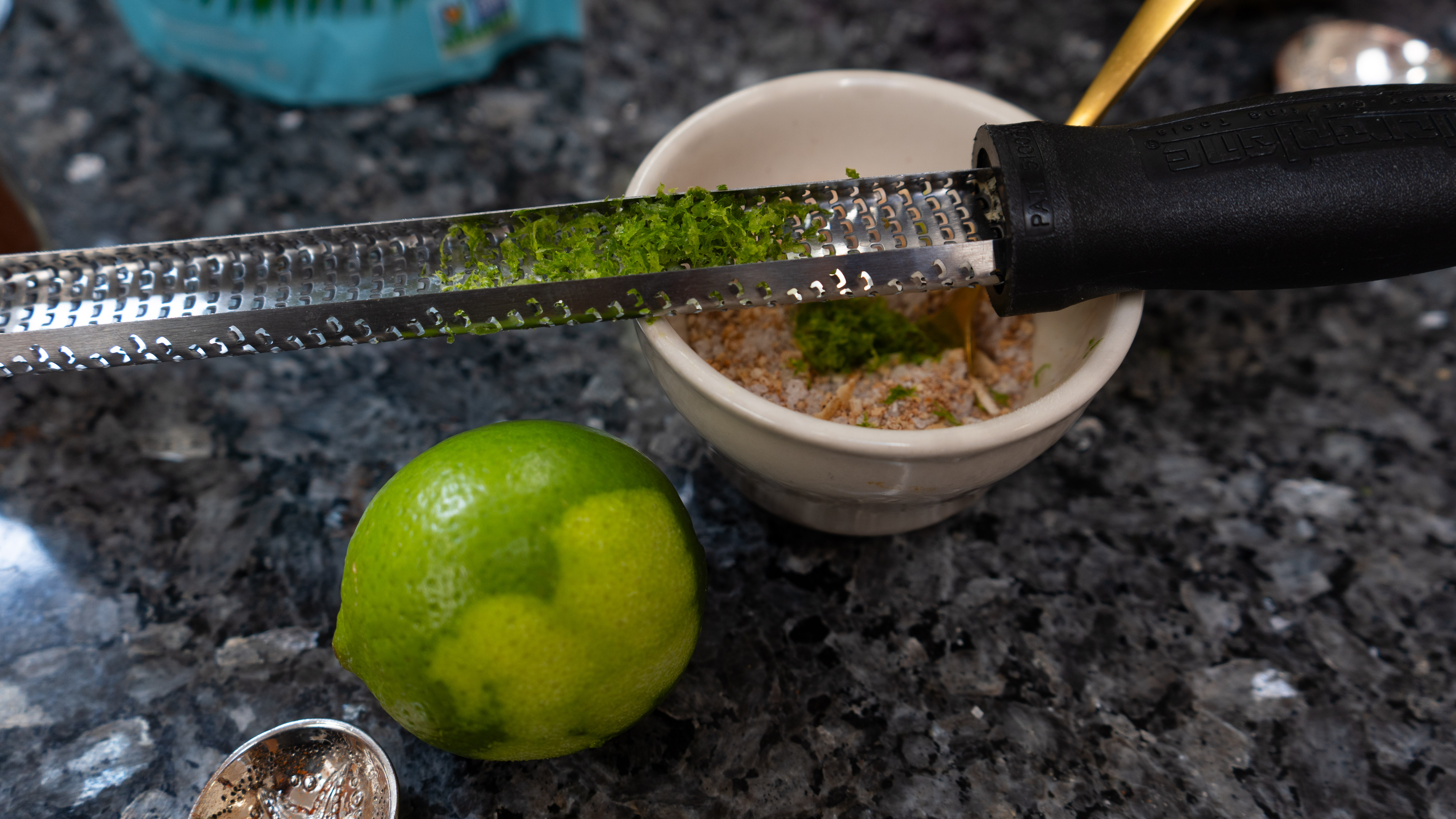 A lime with a zester sitting on a bowl of other herbs and salts