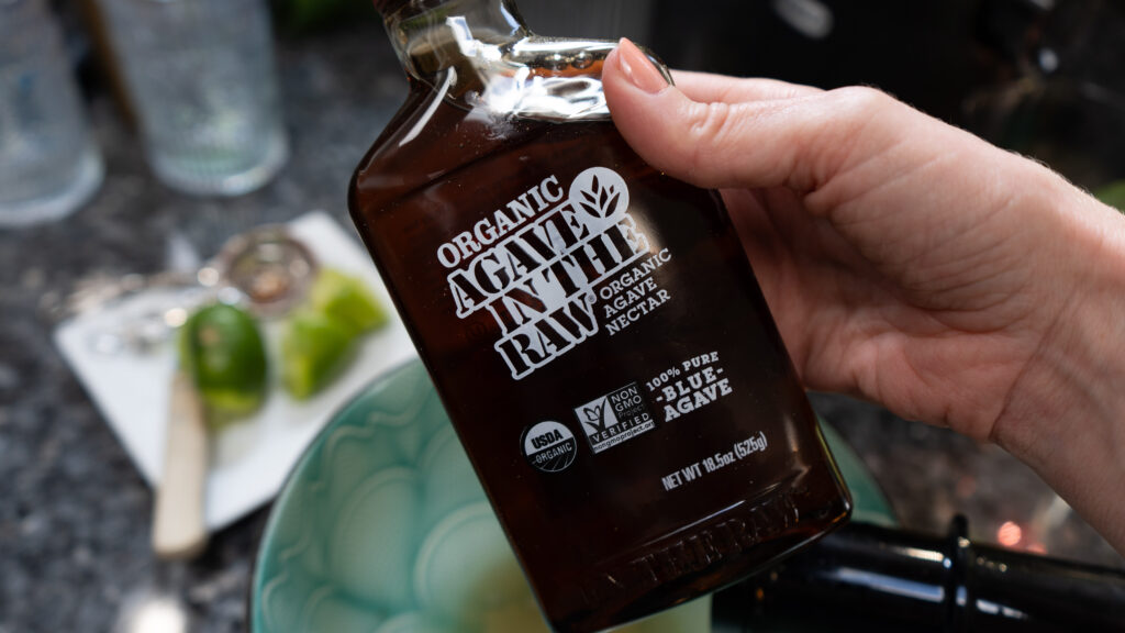 A hand holding a dark bottle that says Organic Agave In The Raw 