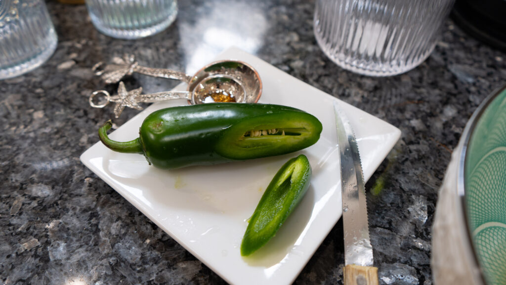 A sliced jalapeño pepper with a knife and measuring spoons on a white plate