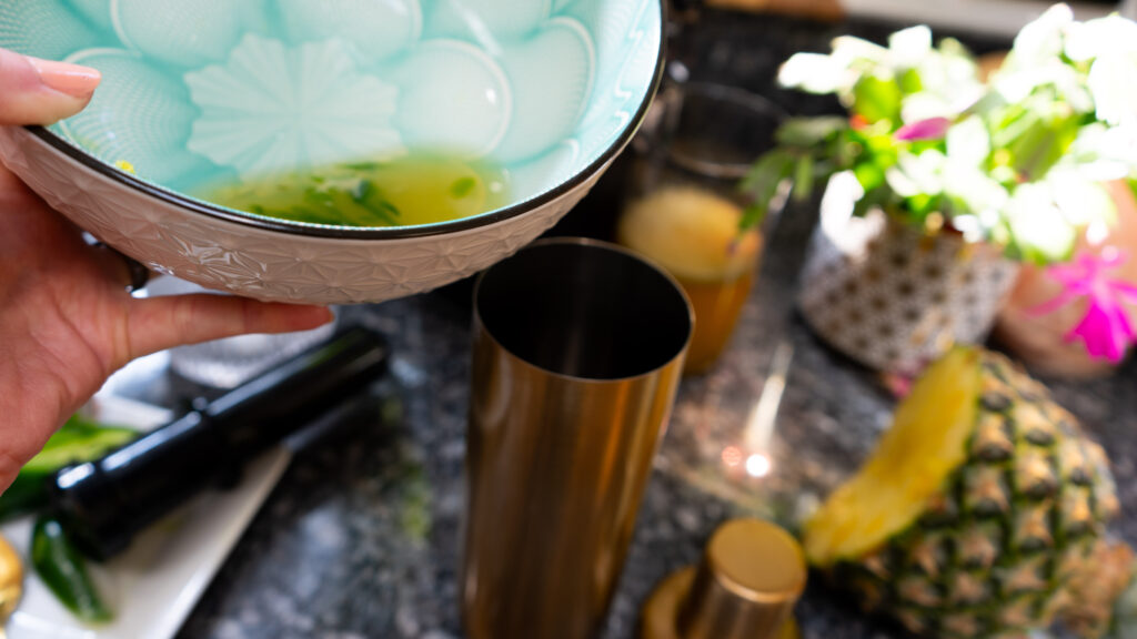 A yellow liquid being poured from a bowl into a gold shaker