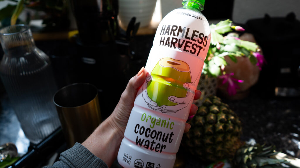 A hand holding a big white bottle that says Harmless Harvest Coconut Water